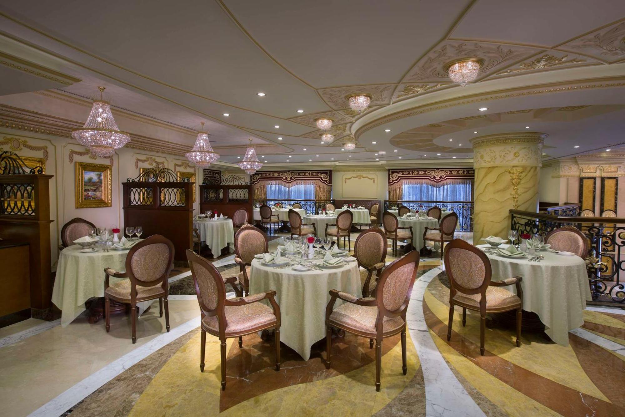 皇家玫瑰酒店 阿布扎比 外观 照片 The photo shows an elegantly decorated restaurant interior. The space features round tables covered with white tablecloths, each set with cutlery and glassware. Stylish, upholstered chairs surround the tables. The lighting is soft, with decorative ch